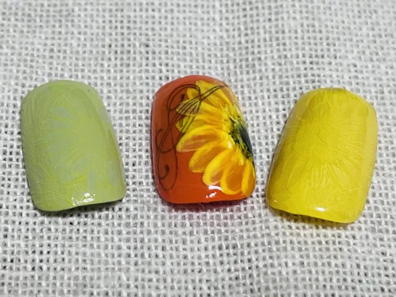 オレンジ色のベースにヒマワリとラインアートが描かれたチップと、淡いグリーン、イエローのチップが並んでいる様子